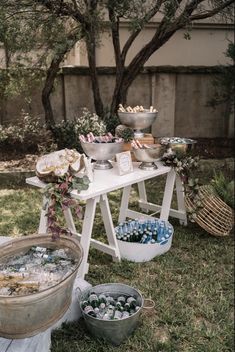 an outdoor party with ice buckets and food on the table in front of some trees