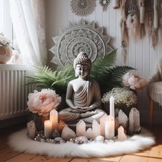 a buddha statue sitting on top of a white rug next to candles and flowers in front of a window