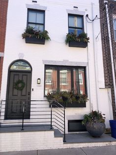 a white brick building with black windows and plants on the balconies above it