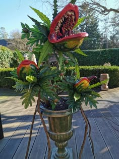 a metal vase filled with flowers on top of a wooden table next to a hedge