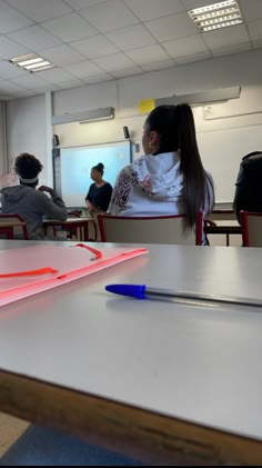 a woman sitting at a table in front of a whiteboard with red and blue markers on it