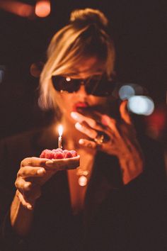 a woman holding a small piece of food in her hand with a lit candle on it