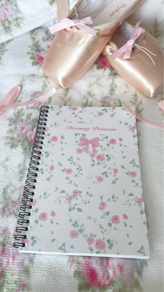 a note book and ballet shoes on a bed with pink floral sheets, bows and ribbons