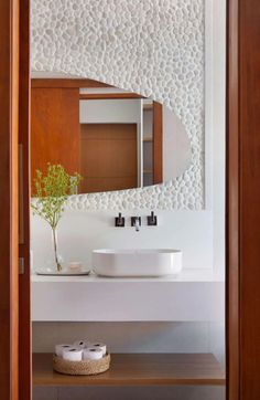 a white sink sitting under a bathroom mirror next to a wooden shelf with two rolls of toilet paper on it