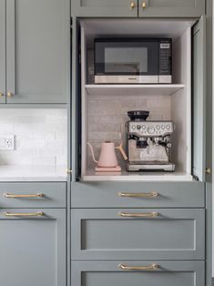 a kitchen with gray cabinets and gold pulls on the handles, coffee maker in the cabinet