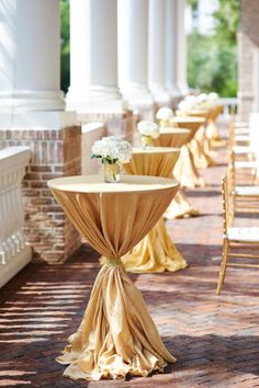 the tables are covered with yellow cloths and white flowers in vases on them