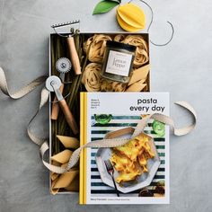 a box filled with pasta and other food items next to a ribbon on the table