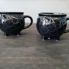 two black coffee mugs sitting next to each other on top of a wooden table