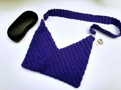 a purple crocheted purse next to a black computer mouse on a white surface