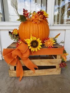 a pumpkin sitting on top of a wooden crate filled with sunflowers and leaves