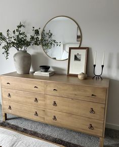 a dresser with a mirror, vase and plant on it in a room that has carpeted flooring