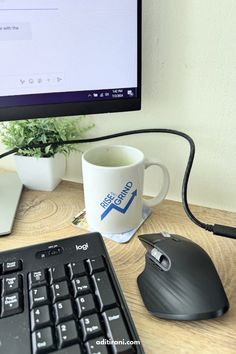 a computer keyboard, mouse and coffee cup on a desk in front of a monitor