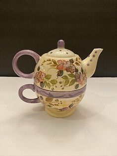 a tea pot with flowers painted on the side and purple trimmings around it