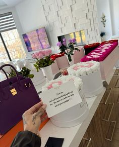 a woman holding up a sign in front of several boxes with flowers on top of them