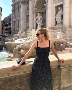 a woman leaning against a wall next to a fountain