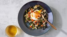 a blue bowl filled with rice and vegetables next to a glass of beer on a white table