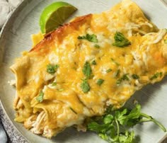 an enchilada on a plate with cilantro and lime