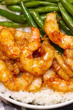 a white plate topped with shrimp and rice next to green beans on top of a table