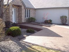 a house that is in the middle of some grass and gravel with bushes around it