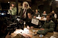 a group of people sitting around a wooden table in front of a camera man holding a sign