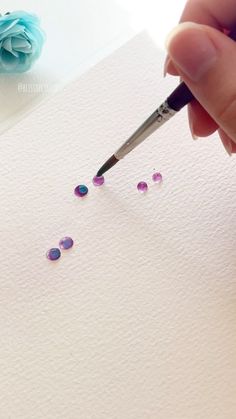 a hand holding a pen writing on top of a piece of paper with tiny beads