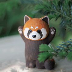 a small toy raccoon sitting next to a pine tree