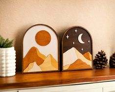 two wooden plaques sitting on top of a table next to a white vase and pine cones