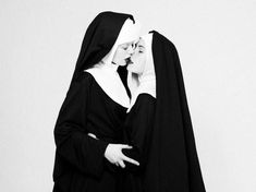 two women dressed in nun costumes kissing each other's foreheads while standing side by side