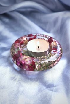 a candle is lit on a glass plate with flowers and leaves in the center, sitting on a bed sheet