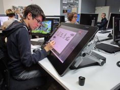 a man sitting in front of a laptop computer on top of a white desk next to other people