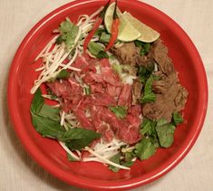 a red plate topped with meat and veggies on top of a white table