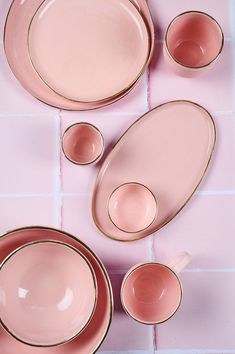 pink and gold dinnerware set with matching saucers, cups and spoons on a pink tile floor