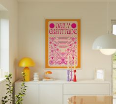 a yellow poster hangs on the wall above a white cabinet and table with vases