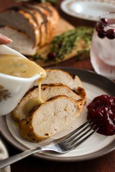 someone is pouring sauce onto some meat on a plate with bread and cranberry sauce