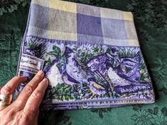 a hand is holding onto a purple and green plaid fabric with birds on it,