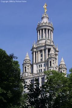 the top of a tall building with a golden statue on it's side and trees in front