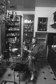 a man sitting at a glass table in a room with shelves and chandeliers