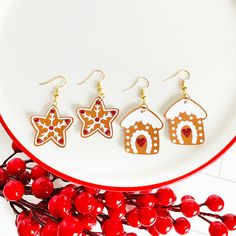 three gingerbread house shaped earrings sitting on top of a white plate next to berries