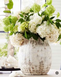 a vase filled with white and green flowers sitting on top of a table next to a window