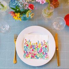 a place setting with flowers on the napkins and gold cutlery next to it