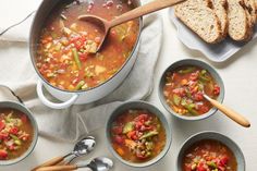 several bowls and spoons filled with soup on top of a white cloth next to slices of bread