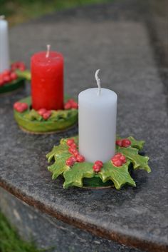 two lit candles sitting on top of a stone table next to holly wreaths and red berries