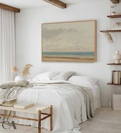 a white bedroom with a large painting hanging on the wall above it's bed