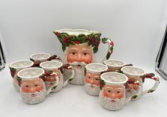 a group of coffee mugs with santa claus's head on top and holly wreath around them