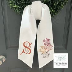 a white scarf hanging on a door with the letter s and leaves painted on it