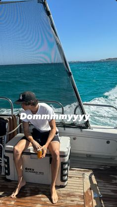 a man sitting on the back of a boat in the ocean while holding a drink