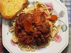 a white plate topped with spaghetti and meat next to a piece of bread on a table