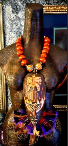 A wild and exotic tribal or ethnic chest piece - statement pendant is yours if you are brave enough to rock such a piece! A earth tone carved wood mask from Bali with a butterfly motif hosts feathers among the bottom portion adding texture and color. An oversized orange-brown Moroccan resin beaded necklace suspends the mask portion. The necklace adjusts from 23-26" and closes with gold tone hardware and a lobster claw clasp. Two ornate Tibetan beads with inlaid turquoise and coral flank the pendant. The pendant measures approximately 13" x 10". This is a surpringly lightweight piece considering all of the components. The back of the necklace is a mix of round coral, wood and gold tone tribal metal spacers. A MUST HAVE for your Autumn wardrobe! From the Atelier of Kat Kouture. Bohemian Hand Painted Necklaces For Festivals, Bohemian Hand Painted Festival Necklaces, Traditional Hand Painted Festival Necklaces, Traditional Hand Painted Necklaces For Festivals, Bohemian Brown Hand Painted Necklaces, Bohemian Hand Painted Brown Necklace, Bohemian Brown Hand Painted Necklace, Carved Amulet Jewelry For Festivals, Luxury Large Bead Amulet Jewelry