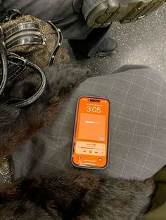 an orange cell phone sitting on top of a bed next to a handbag and purse