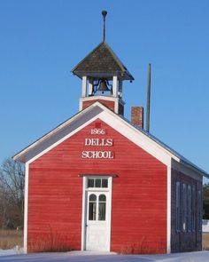 an old red building with a bell tower and snow on the ground in front of it